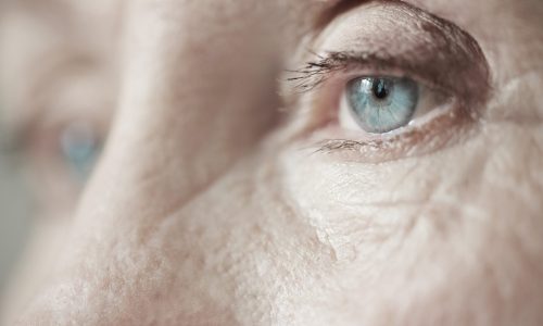 Extreme close-up shot of sad blue eyes on wrinkled female face looking into the distance